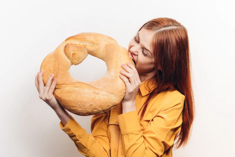 Мучное изделие, буханка и женщина в желтой рубашке на заднем плане, светлый фон, обрезанный вид