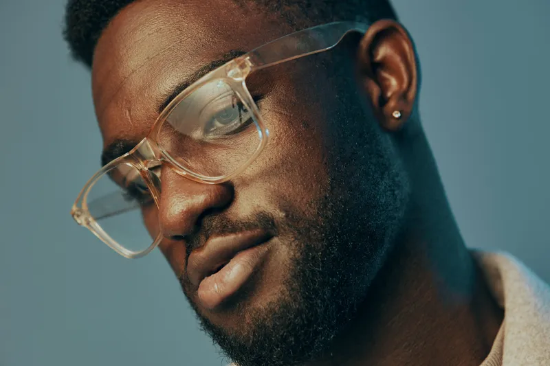 Close up portrait of an African American man wearing stylish glasses, showcasing a confident expression with a soft blue background, reflecting contemporary fashion