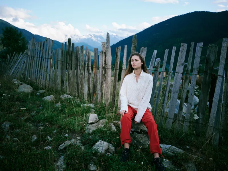 Mountains, fence, woman, outdoor nature calm solitude landscape casual relaxed mood, rustic setting with rocky ground and alpine scenery, white shirt red pants, serene connection with the environment