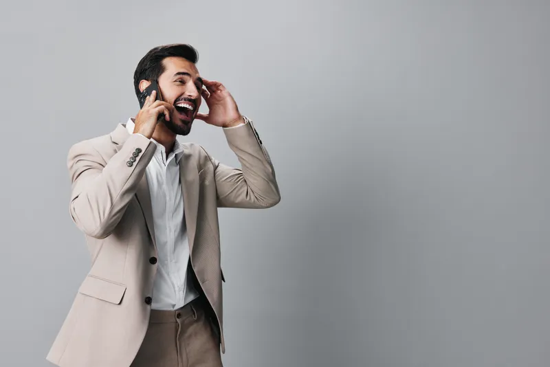 Уверенный в себе мужчина в деловом костюме улыбается и держит в руке смартфон