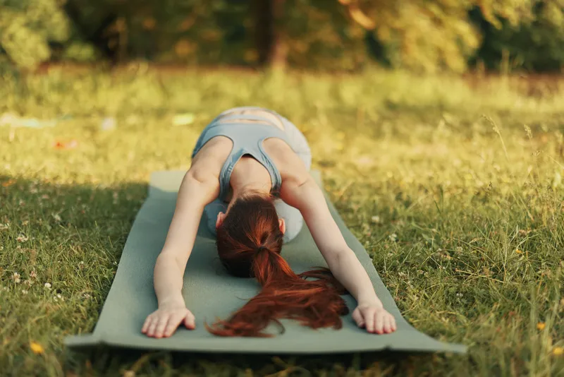 Young woman practicing yoga outdoors in a serene park, displaying tranquility and focus in a healthy lifestyle setting surrounded by nature