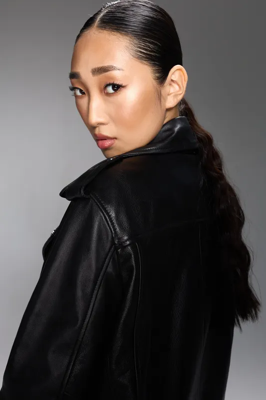 Азиатская женщина в чёрной кожаной куртке, с хвостиком, позирует перед камерой