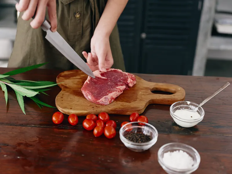 Женщина с ножом в руке режет мясо для жарки на кухне