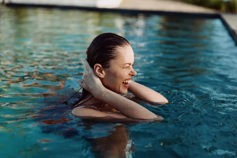 Young woman enjoys swimming in outdoor pool smiles happily holds hair back during sunny day relaxed lifestyle concept summer vacation leisure activity.