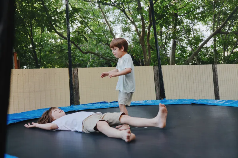Two playful boys enjoying a sunny day on a trampoline, laughing and having fun outdoors in a lush green garden. Perfect for children's activity themes.