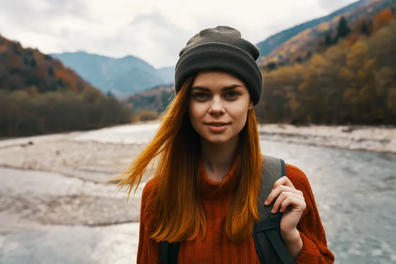 Красивая женщина в свитере с рюкзаком в горах у реки на природе, портрет
