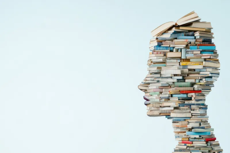 Уникальный профильный силуэт, составленный из стопок книг, символизирующий стремление к знаниям и образованию на мягком пастельном фоне