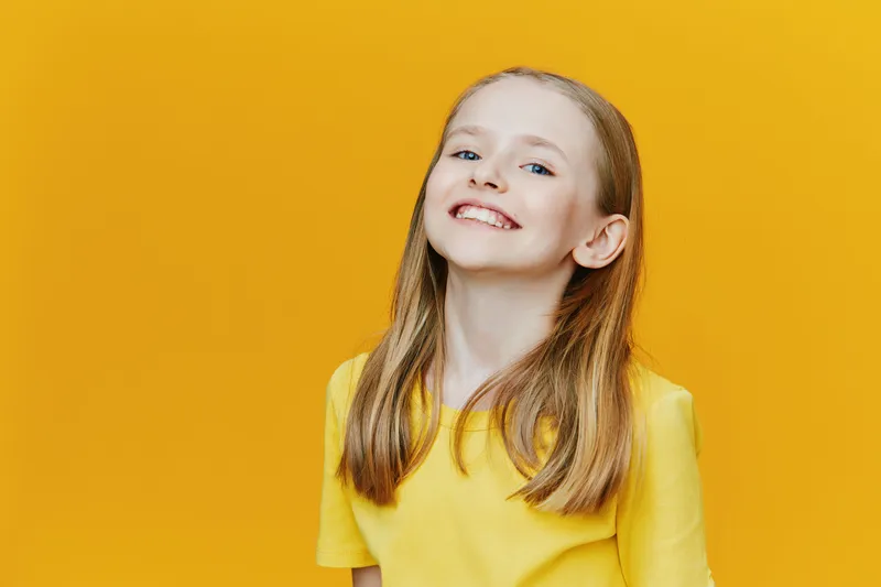 Happy girl with long hair in a bright yellow shirt smiling against a vibrant yellow background, showcasing joy and confidence, perfect for cheerful lifestyle themes