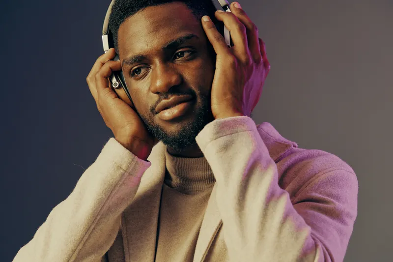 Young man enjoying music in headphones, wearing a stylish sweater, with a confident expression, set against a colorful gradient background
