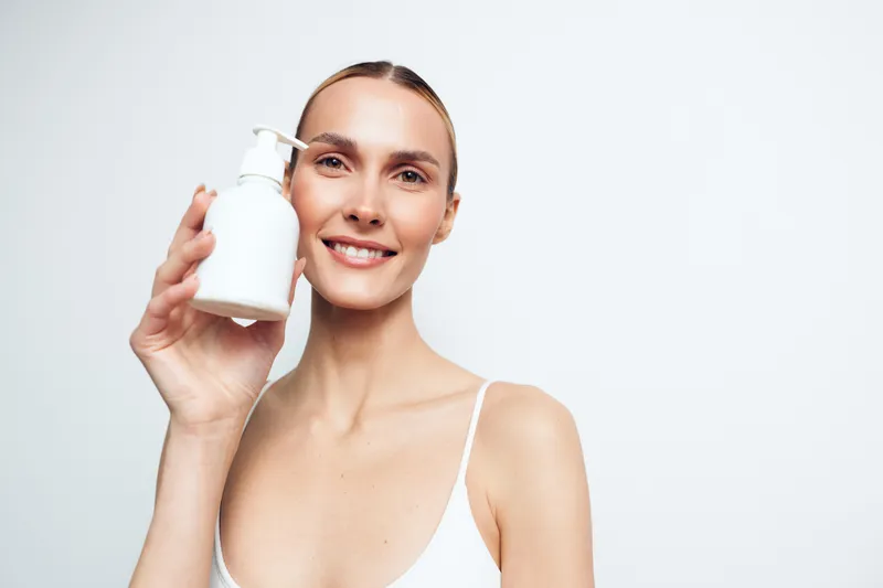 Smiling woman holding a white cup, clean studio portrait on white background, gentle skincare routine idea, hydration and wellness concept, soft natural light, minimal composition
