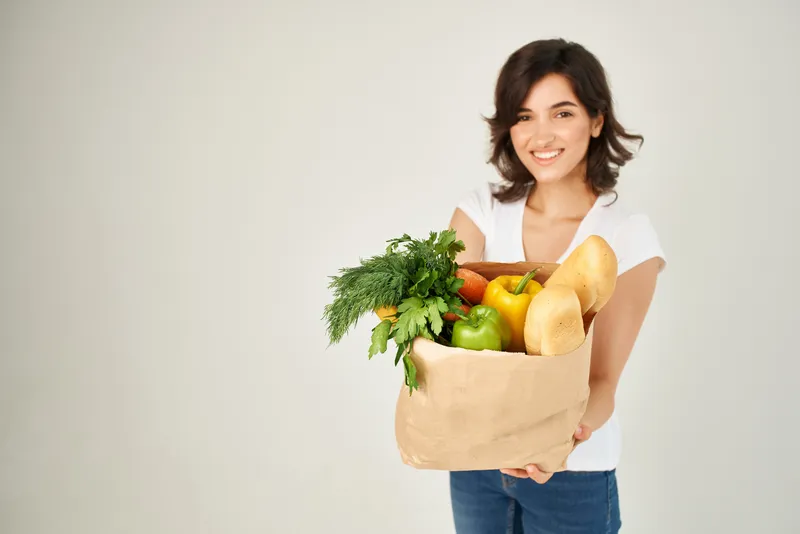 Весёлая брюнетка с бумажным пакетом продуктов и овощей