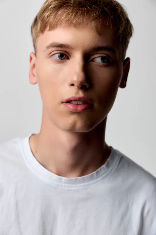 Young man, close up, studio, thoughtful, neutral background, white shirt, calm expression and clear skin convey a clean, modern look suitable for fashion, lifestyle, or creative industry projects