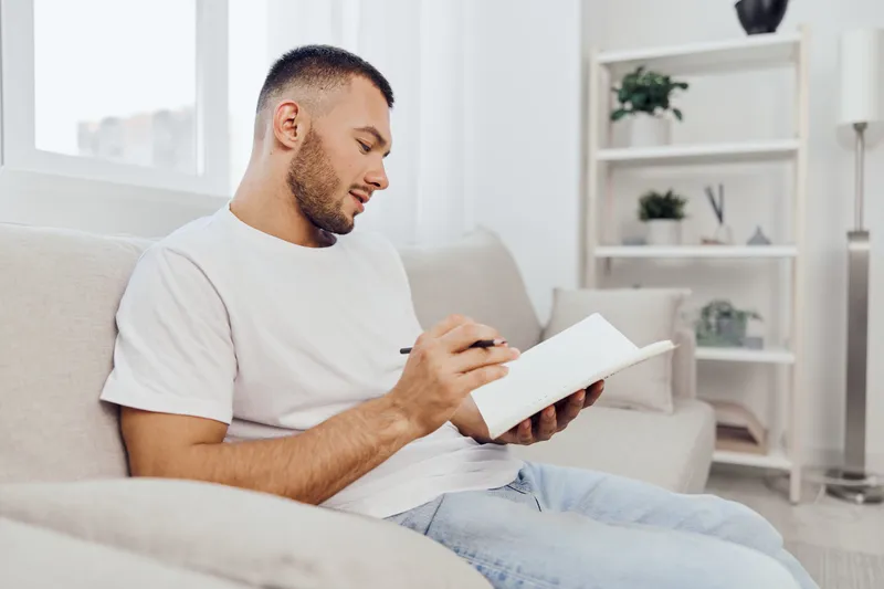 Thoughtful man writing in a notebook, surrounded by a tranquil home environment, capturing the essence of creativity and mindfulness in modern living.