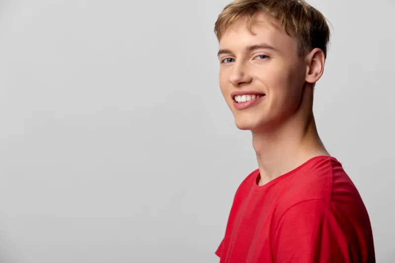 Young man wearing a red shirt smiles in a bright studio setting with a neutral background, showcasing casual confidence and approachable style for lifestyle, fashion, or headshot photography visuals