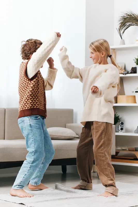 Two children in a cozy livingroom throw pillows at each other, capturing spontaneous joy, playful energy, and a bright, candid indoor moment of simple friendship and imagination.