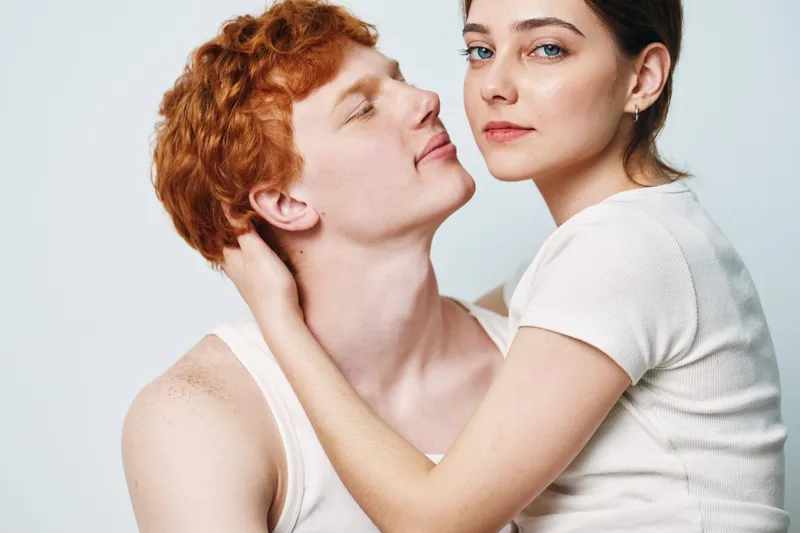 Couple, young man and woman with fair skin embracing in tender moment, intimate pose and closeup portrait on light background expressing affection and connection between two people.