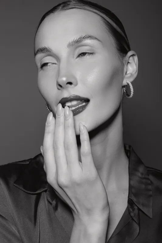 Portrait of a young white woman with fair skin and slicked hair posing with hand near lips in moody black and white studio portrait fashion concept.