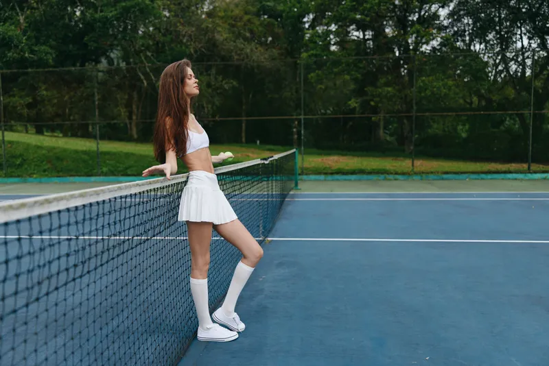 A young woman in sporty attire resting on a tennis court, showcasing confidence and calmness against a lush green backdrop, ideal for sports themes