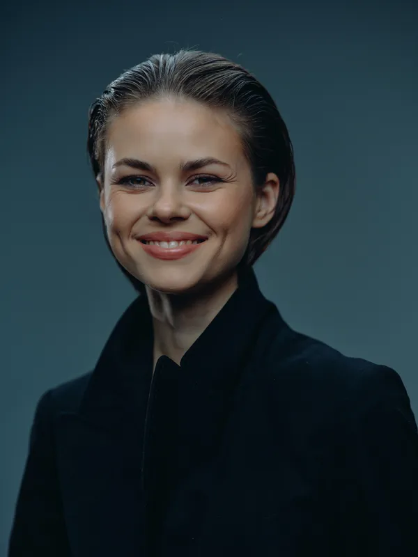 Smiling woman in dark jacket with sleek hair, calm expression, studio portrait, minimal background, modern style.