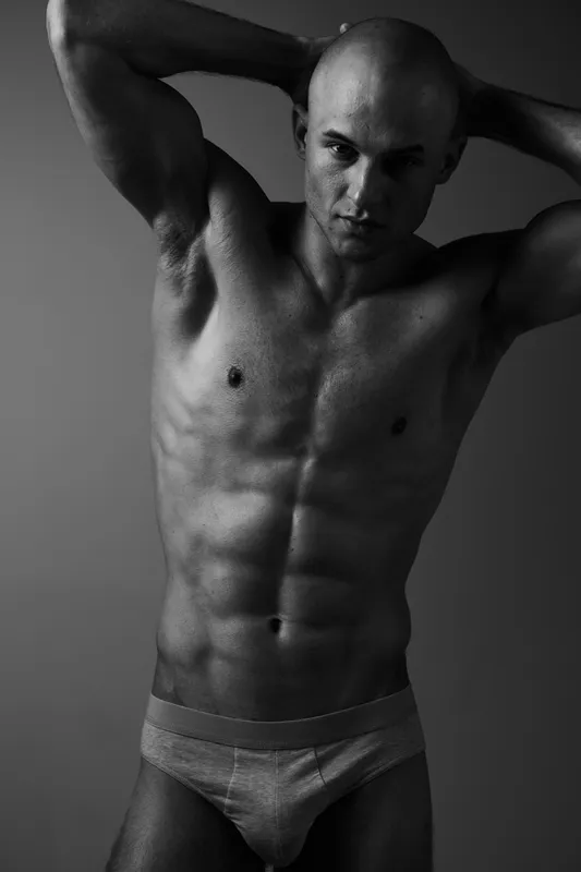 Muscular man posing in black and white, showcasing his physique and confidence, with a dynamic expression and dramatic lighting that emphasizes form. ###
