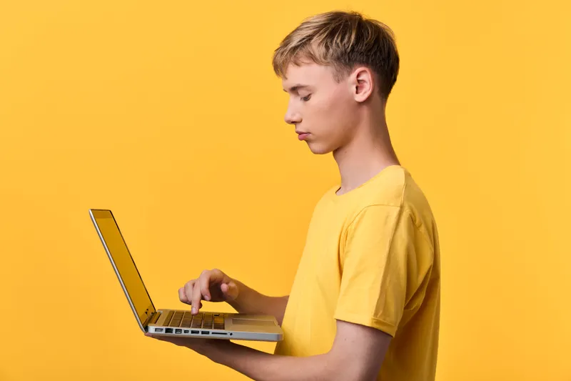 Laptop, man in yellow shirt focused on screen for online learning and technology tasks in a bright studio setting, showcasing digital work and concentration