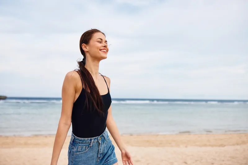 Девушка идёт по пляжу на рассвете, улыбаясь и наслаждаясь моментом