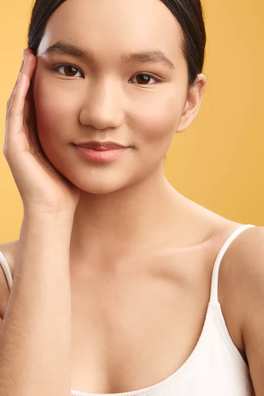 Asian woman portrait in a soft studio setting. She wears a light top, displays a calm smile, and relaxed posture, conveying warmth, confidence, and approachable professionalism.