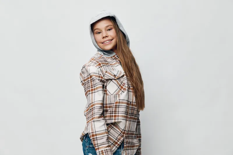 Teenage girl wearing plaid shirt and hoodie smiling confidently with long hair casual style isolated on light background. Youth, happy, fashion and portrait.