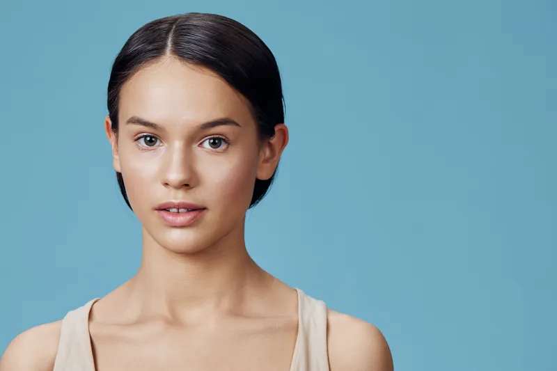 Young woman with short hair and natural makeup against a soft blue background, exuding confidence and calmness, perfect for beauty and wellness concepts
