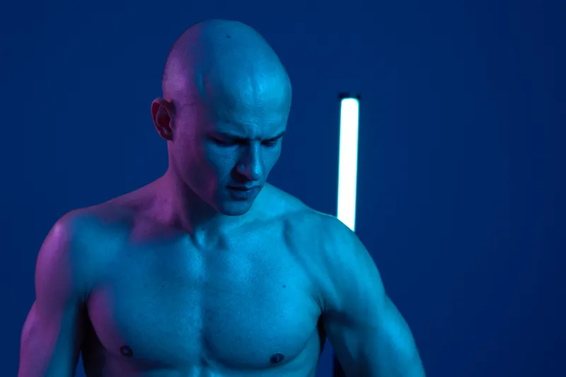 Muscular man in dramatic lighting, showcasing strong features and a contemplative expression, emphasizing the play of colors in this captivating image.