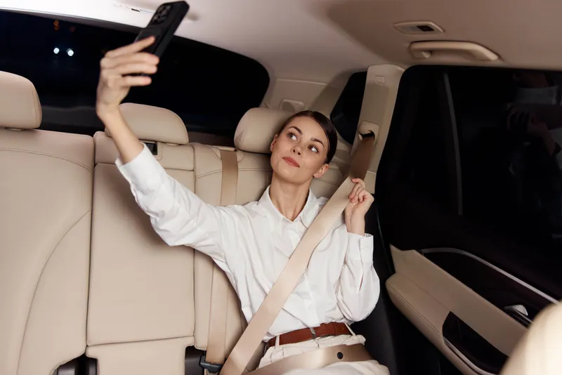 Женщина в автомобиле делает фото на смартфон через окно, запечатлевая искренний дорожный момент и использование технологий