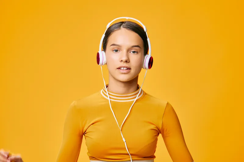 Athletic woman in orange workout top wearing headphones against a vibrant yellow background, ready for a fitness session with focused expression, energy and motivation in a modern studio vibe.