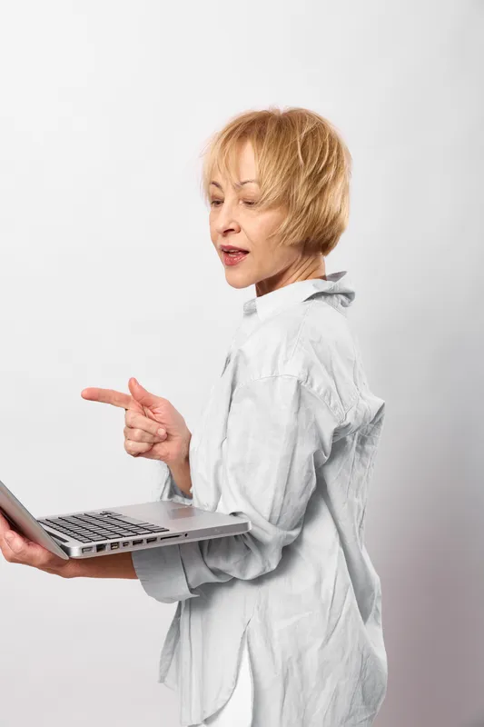 Woman with short hair working with laptop and phone, pointing toward screen in business communication, minimal studio background, soft lighting, focused expression, technology and office work