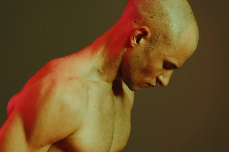 Portrait of a focused man with a shaved head, showcasing strength and determination, bathed in soft red light against a contrasting dark background.