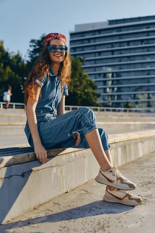 lifestyle woman in modern boho-western denim street style with sunglasses and bandana, relaxed and smiling under natural sunlight in urban outdoor setting, film color