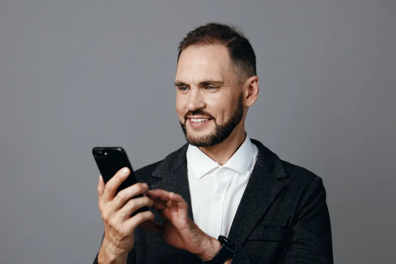 A professional man in a blazer engages with a smartphone, exuding confidence and focus against an isolated colored background, suggesting modern business and clear intent.