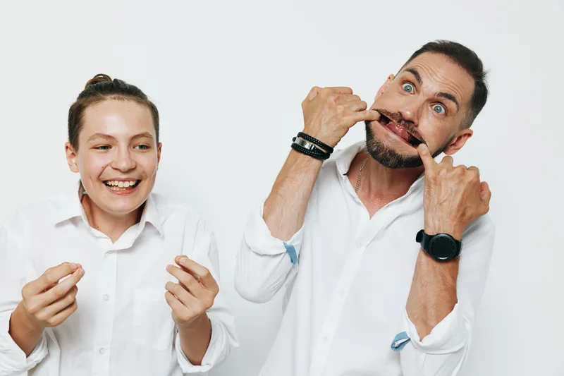 A professional man in business attire on an isolated white background, presenting confident and playful emotion while a teammate smiles nearby.