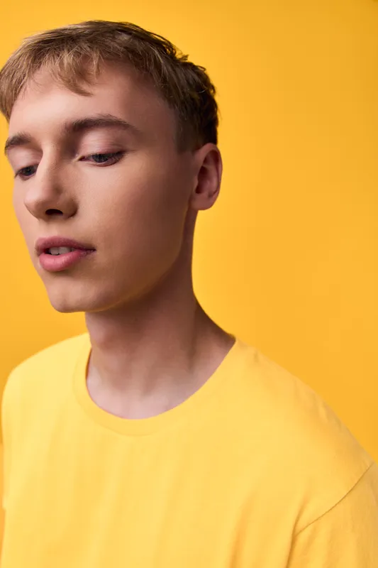 Yellow shirted male in a close-up studio shot, soft lighting highlighting skin tones and calm expression, minimal fashion mood, clean background, modern casual style