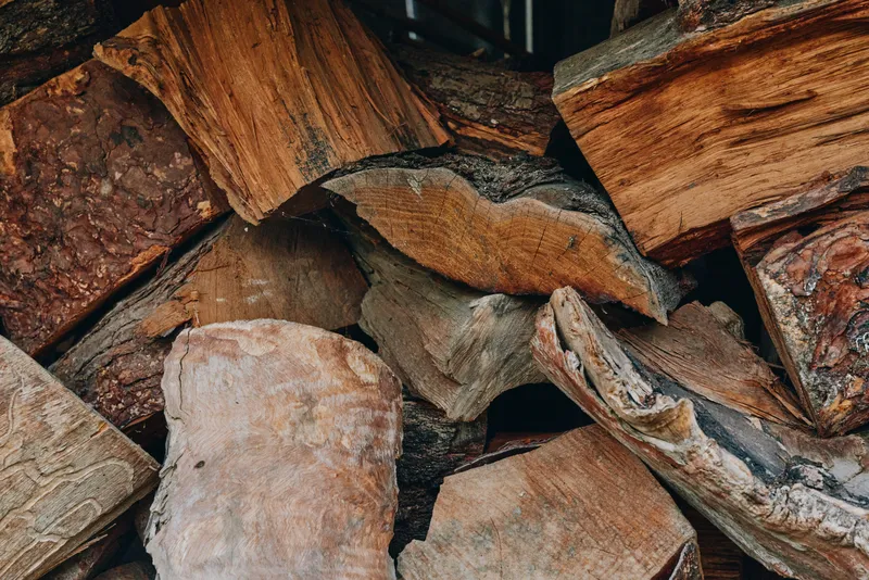 Firewood stacked wood logs split wood pile timber bark rustic closeup of seasoned hardwood in an outdoor shed, textured grain and brown tones, heating fuel for fireplace and cozy winter prep.