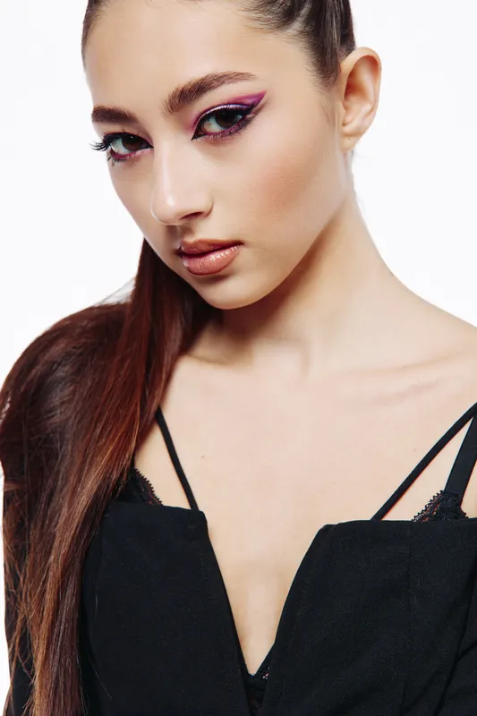 Close-up portrait of a young woman with glossy sleek hair and bold graphic eyeliner in a black outfit against white. Creative beauty and fashion studio concept.