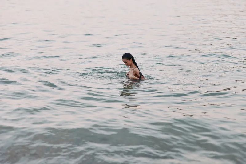 Woman swimming peacefully in calm water with soft pastel colors and serene mood during a quiet moment in nature.