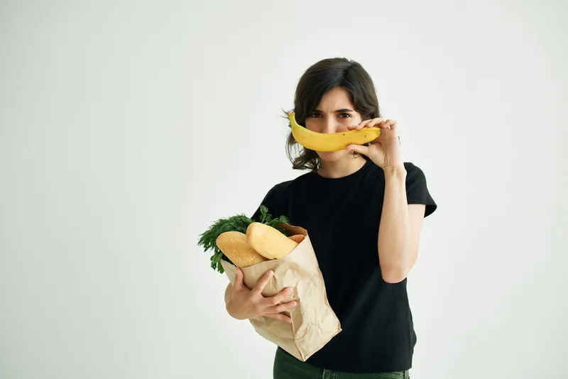 Весёлая брюнетка с сумкой для продуктов готовит здоровую пищу