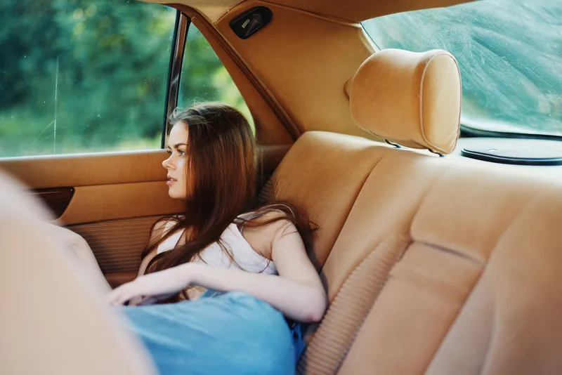 Pensive young woman in a vintage car, reflecting on life with thoughtful expression amidst warm, earthy tones. Ideal for emotional storytelling and vintage themes.