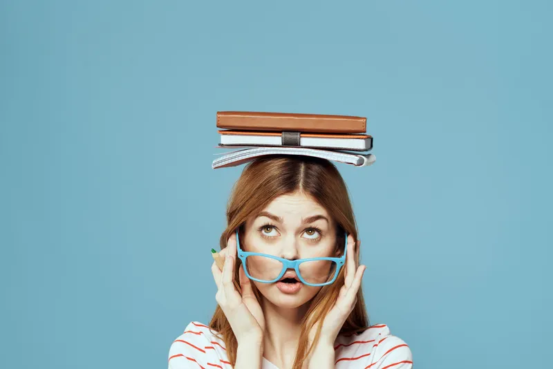 Студентка с книгами на голове, наука, образование, синий фон, эмоции, жестикуляция руками