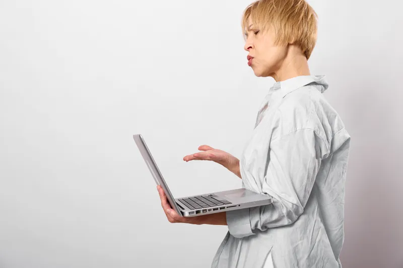 Woman holding a laptop in studio with white background, business communication gesture, serious profile expression, clean minimal setting, ready for remote work