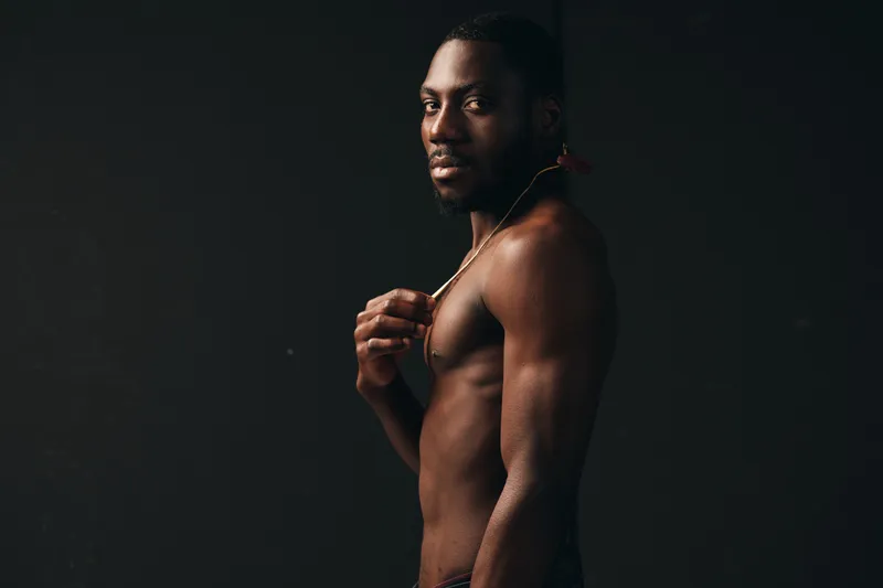 African man with muscular body and creative concept posing shirtless in studio with dark background, visual style emphasizing strength and confidence in portrait.