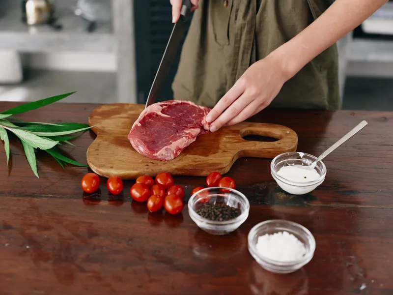 Женщина с ножом в руке нарезает стейковое мясо для жарки на кухне