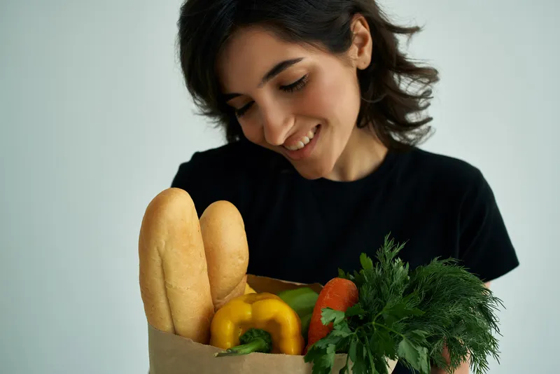 Весёлая женщина в чёрной футболке, пакет с продуктами, овощи, здоровая еда, крупный план