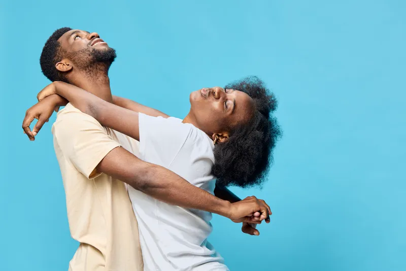 Happy young couple embracing each other against a blue background, showcasing joy and love, wearing casual light colored clothing, celebrating their bond