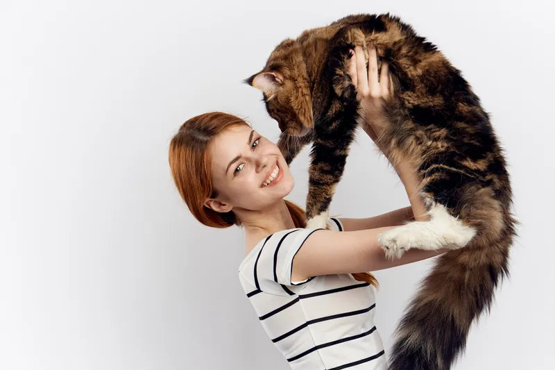 Рыжеволосая женщина держит в руке кота, полосатая футболка, светлый фон, домашний питомец